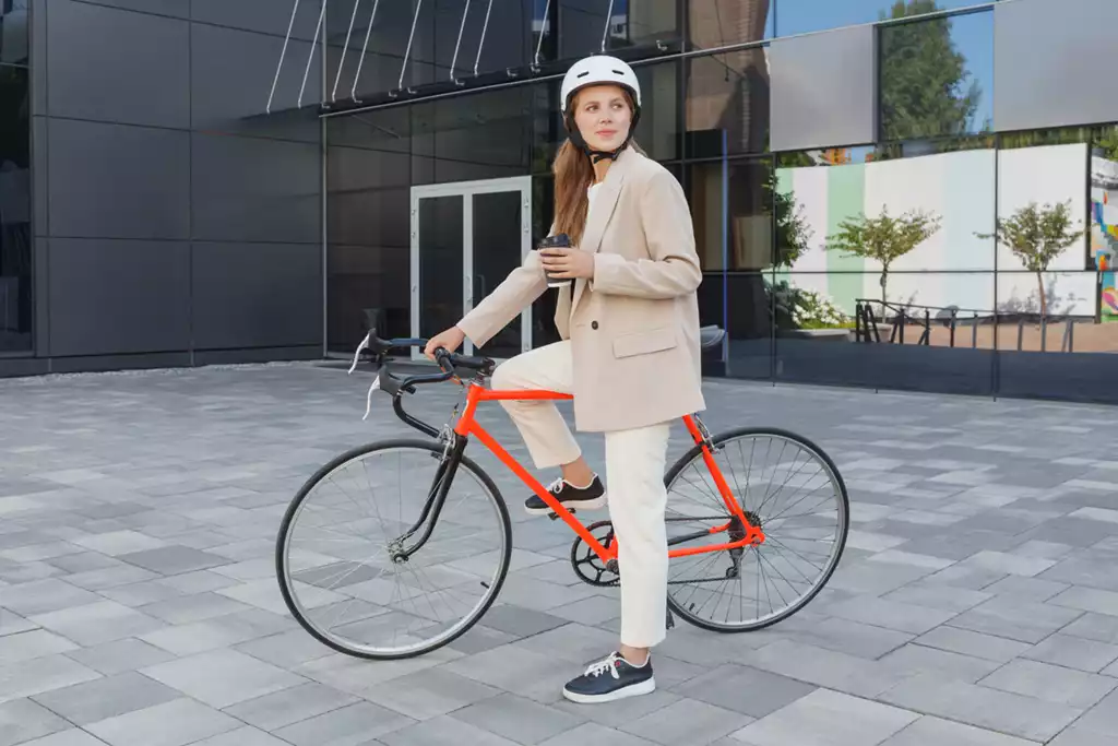 ヘルメットを被って自転車に乗りながらコーヒーを持つ女性