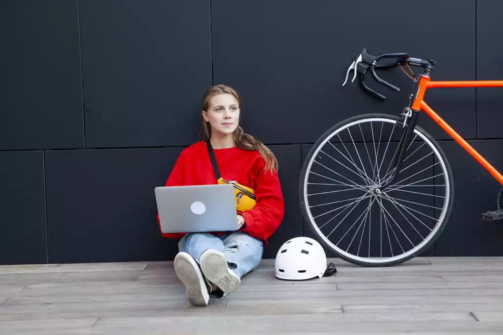 自転車とヘルメットのそばでパソコンの作業をする女性