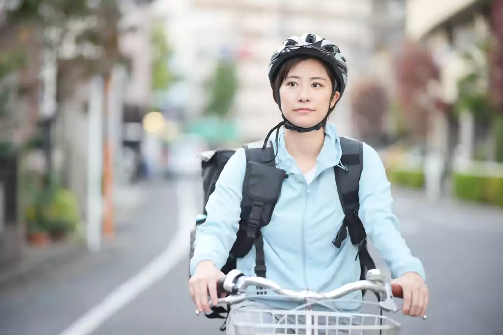 ヘルメットを被って自転車に乗るフードデリバリーの女性